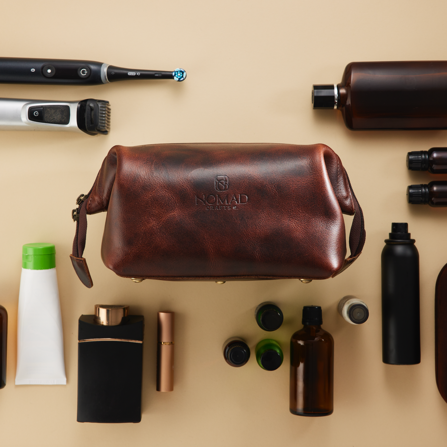 Collection of grooming products including a leather bag, bottles, and tools on a beige background