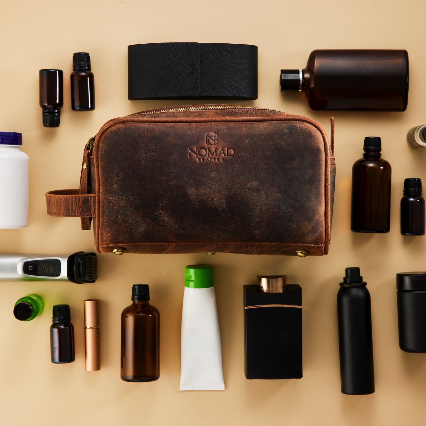 Collection of grooming products including a brown leather toiletry bag with 'Nomad' branding on a beige background.