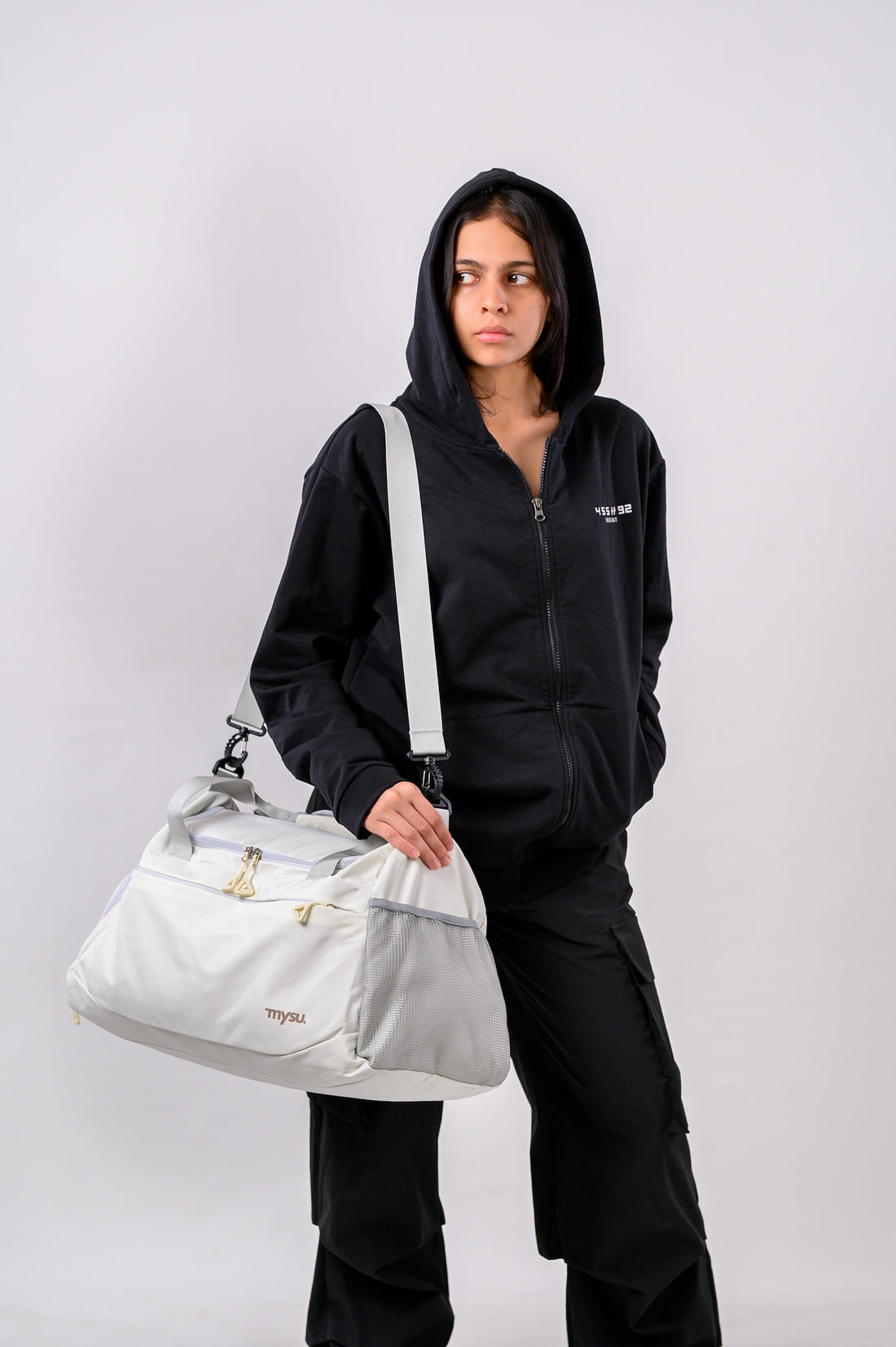 Person wearing a black hoodie and pants holding a white bag against a plain background