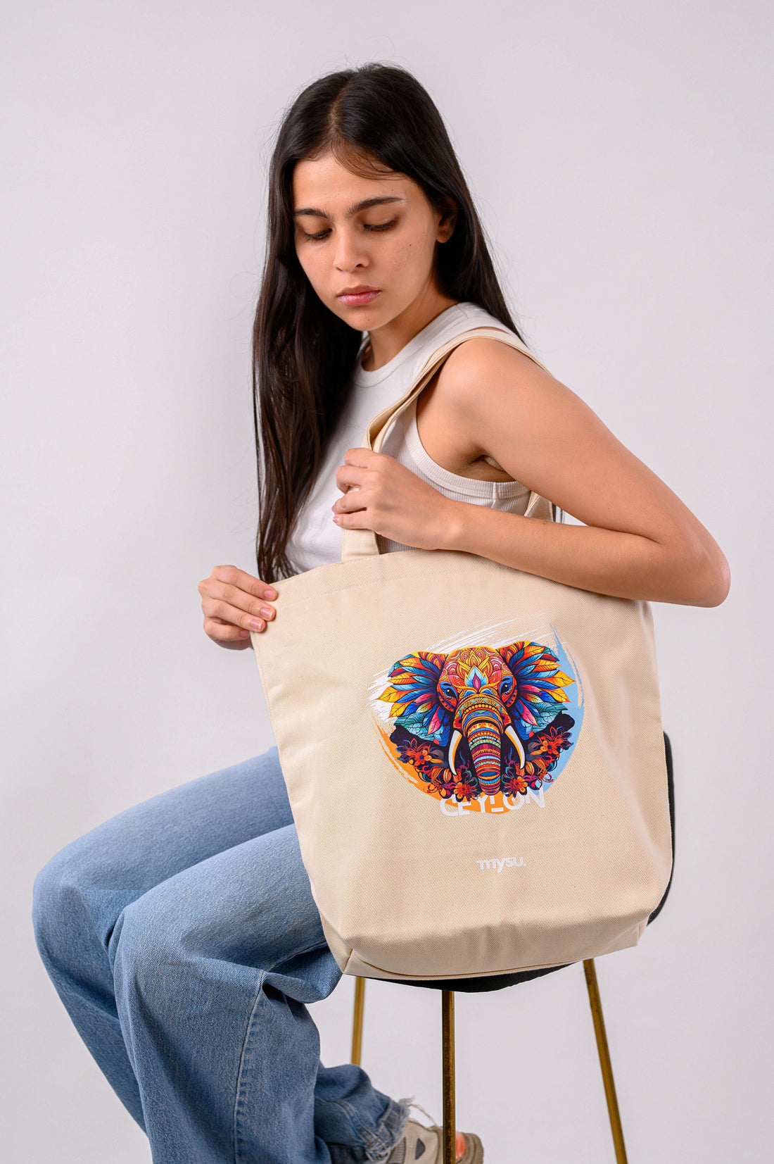 Woman holding a beige tote bag with a colorful elephant design on a white background